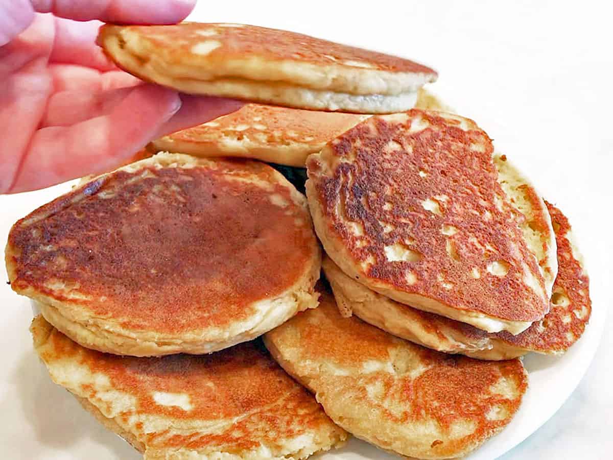 A hand holding a pancakes to show how thick it is. 