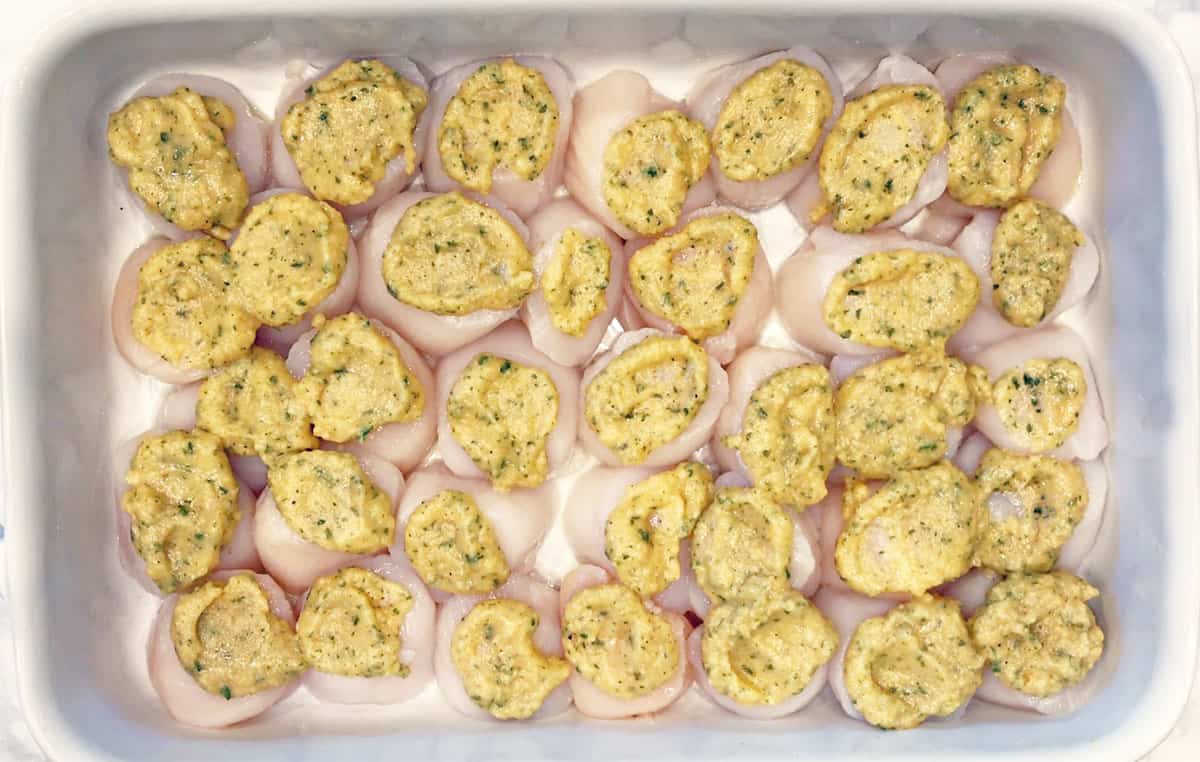 Scallops in a baking dish, topped with a buttery mixture. 