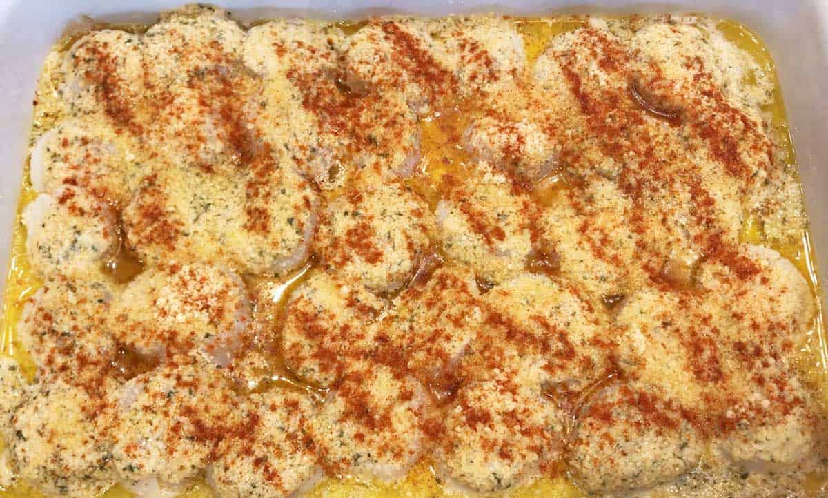 Scallops in a baking dish, sprinkled with parmesan and paprika. 