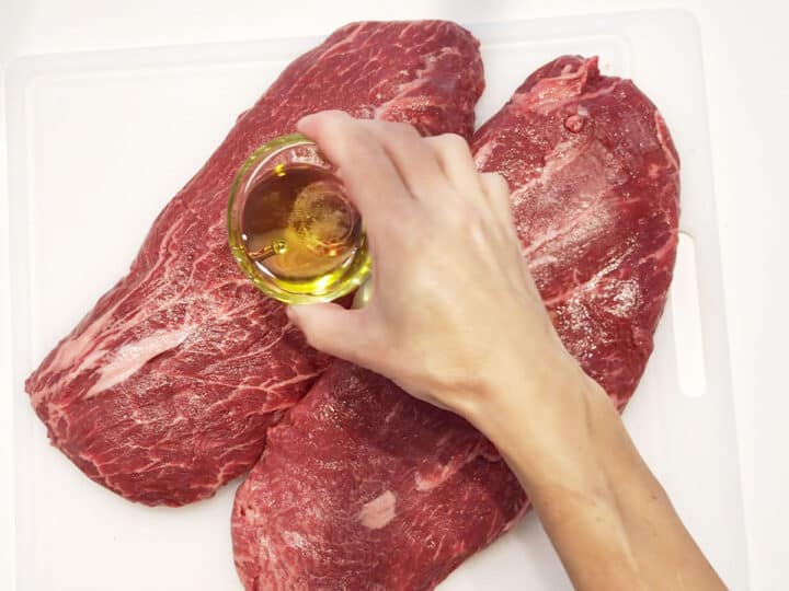 Coating flat iron steaks with olive oil.