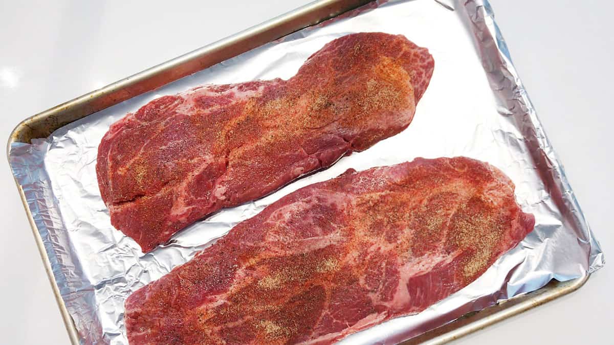 Two flat iron steaks on a foil-lined baking sheet. 