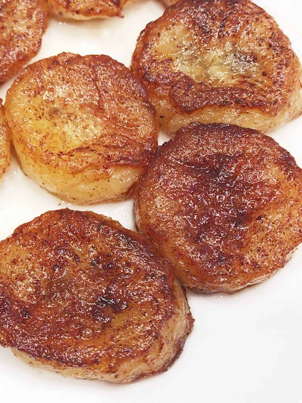 Fried bananas are served on a white plate. 