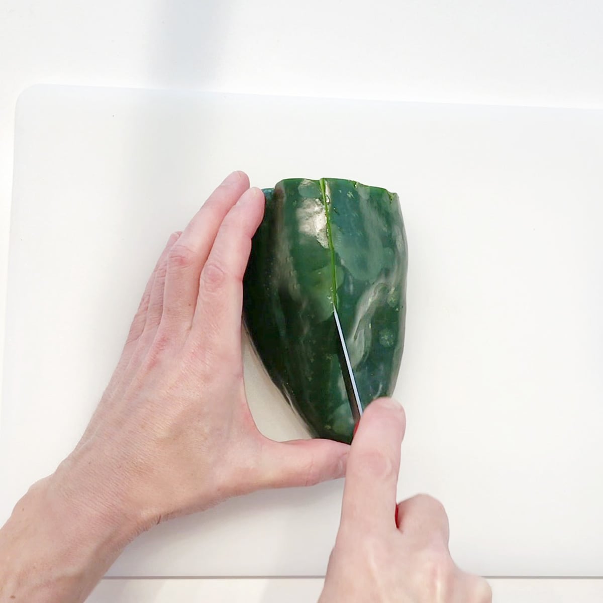 Cutting a slit down the side of a poblano pepper. 