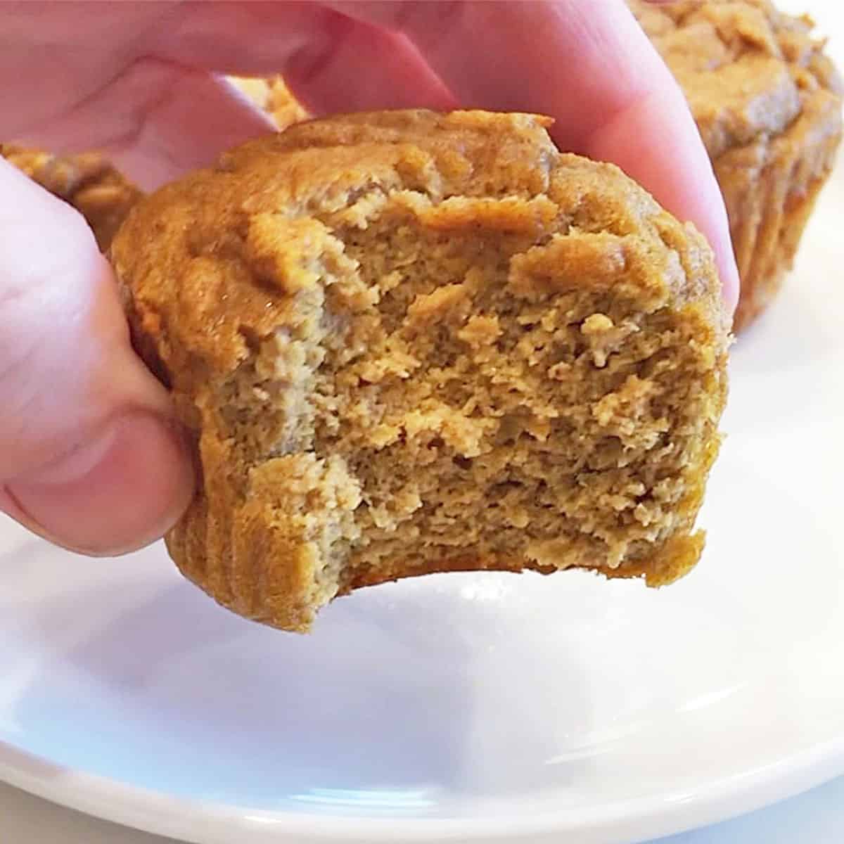 A hand holding a keto pumpkin muffin with a bite. 