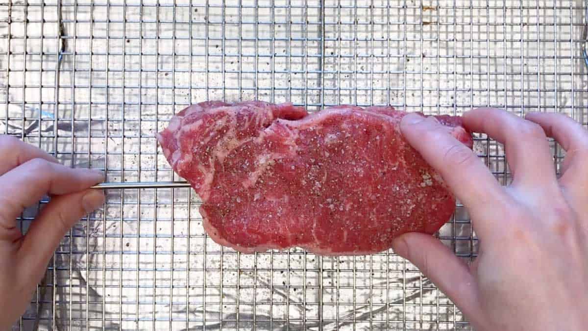 Putting a thermometer into a raw steak before baking. 