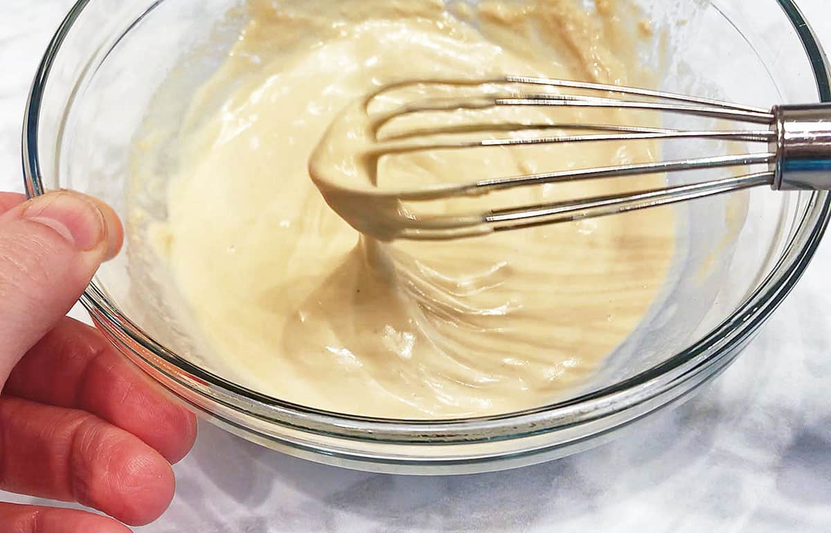 A close-up of tahini sauce in a bowl with a whisk, showing its creamy consistency. 