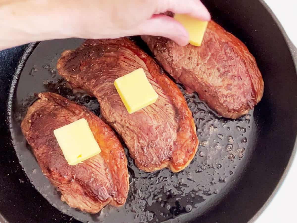 Topping the cooked steaks with butter. 