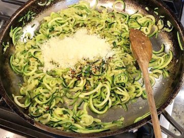 Adding spices and parmesan to the zucchini noodles in the skillet.