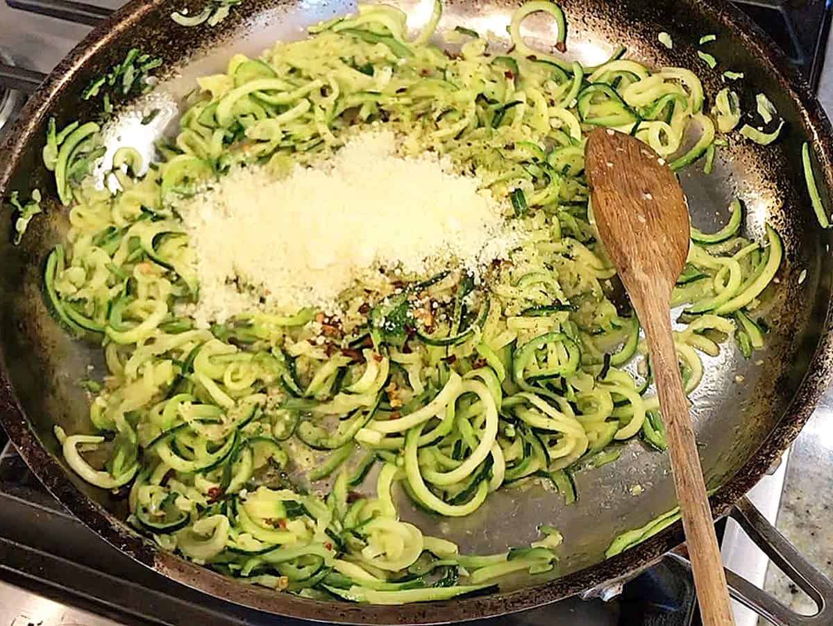 Adding parmesan and spices to the zoodles in the skillet. 