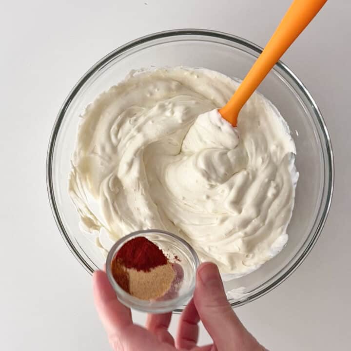 Adding spices to cream cheese in a bowl.