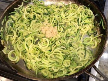 Adding garlic to the zoodles in the skillet.