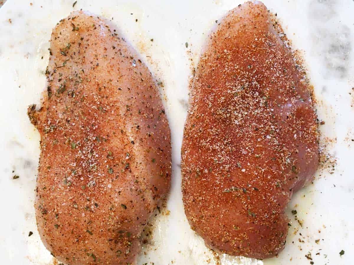 Two raw chicken breasts coated with spices. 
