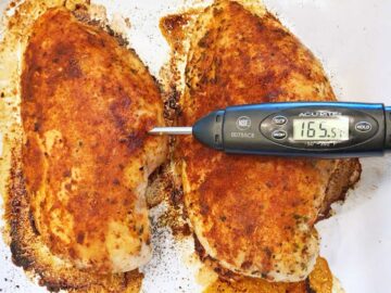A thermometer inserted into a chicken breast showing an internal temperature of 165°F.