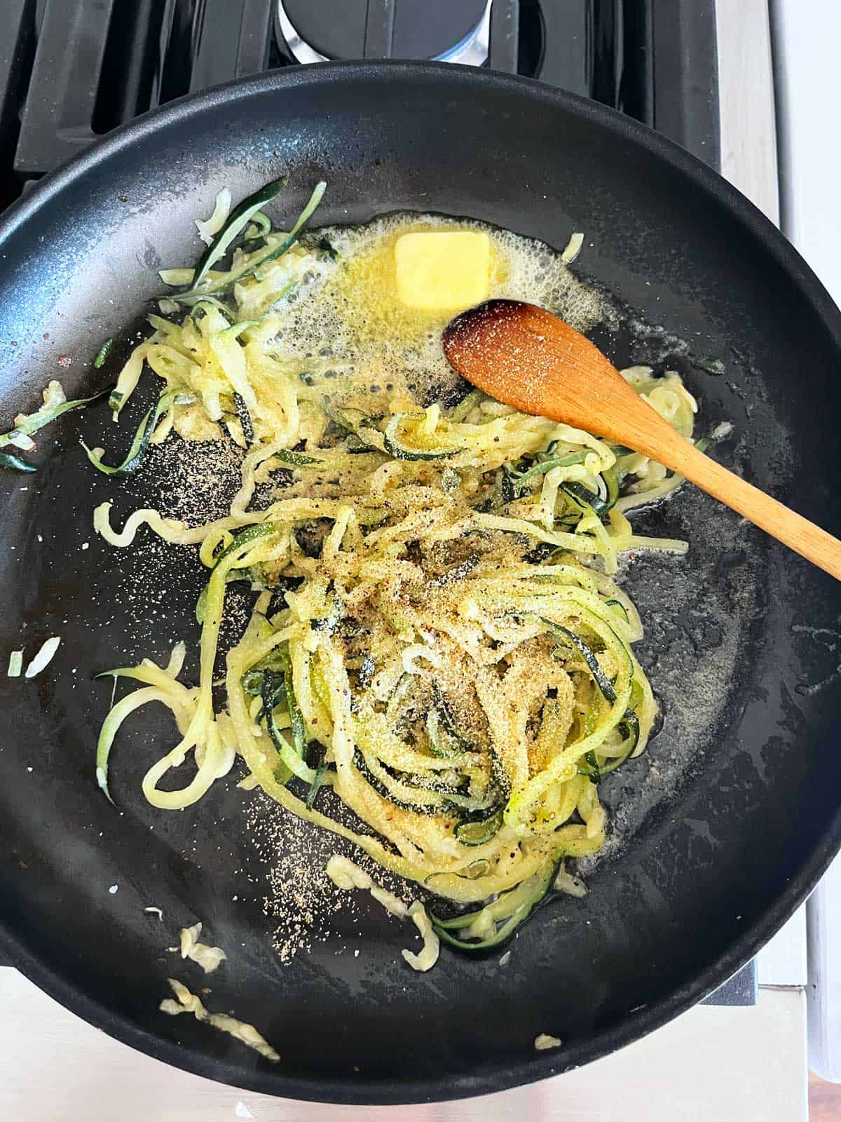 Frozen zucchini spirals in a skillet with butter and seasonings. 