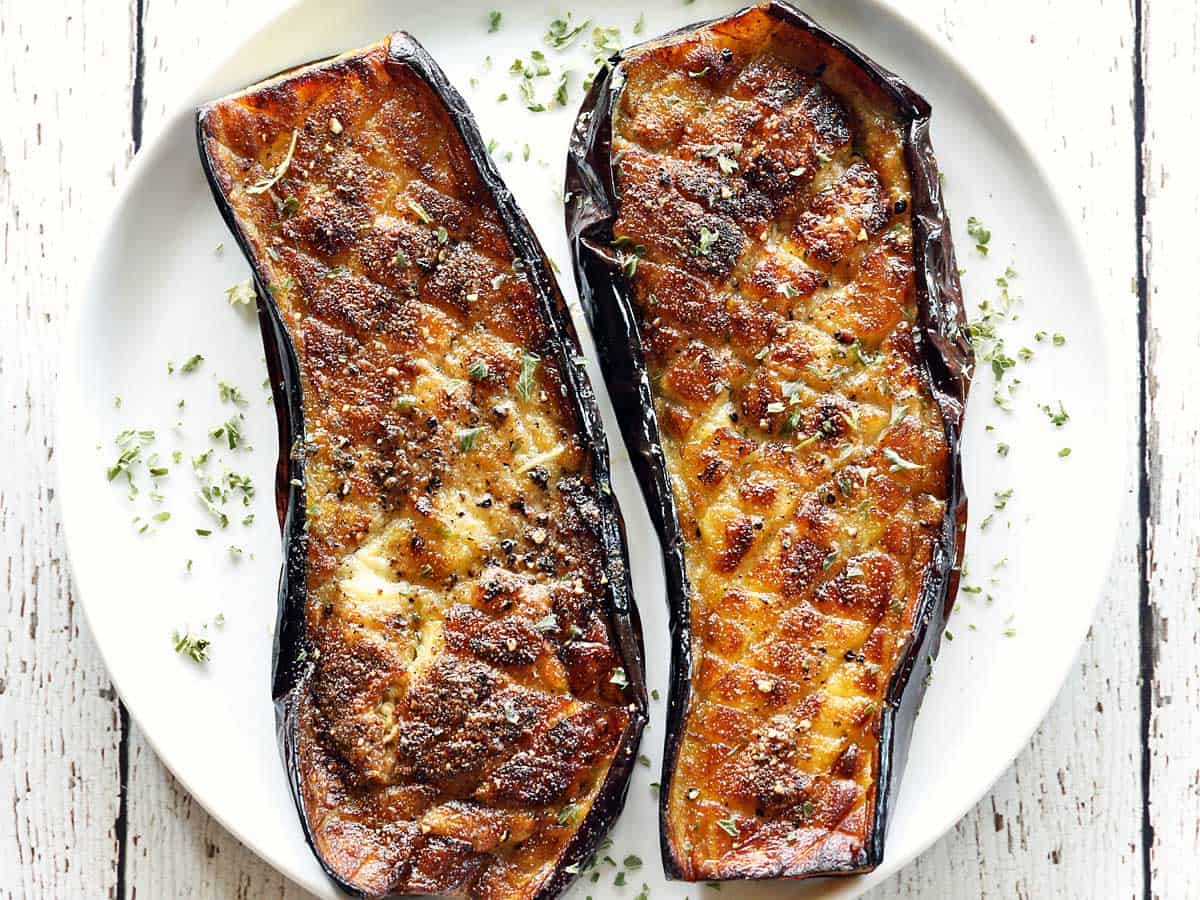 Roasted eggplant is served on a white plate. 