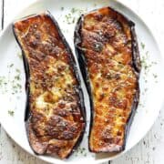 Roasted eggplant is served on a white plate.