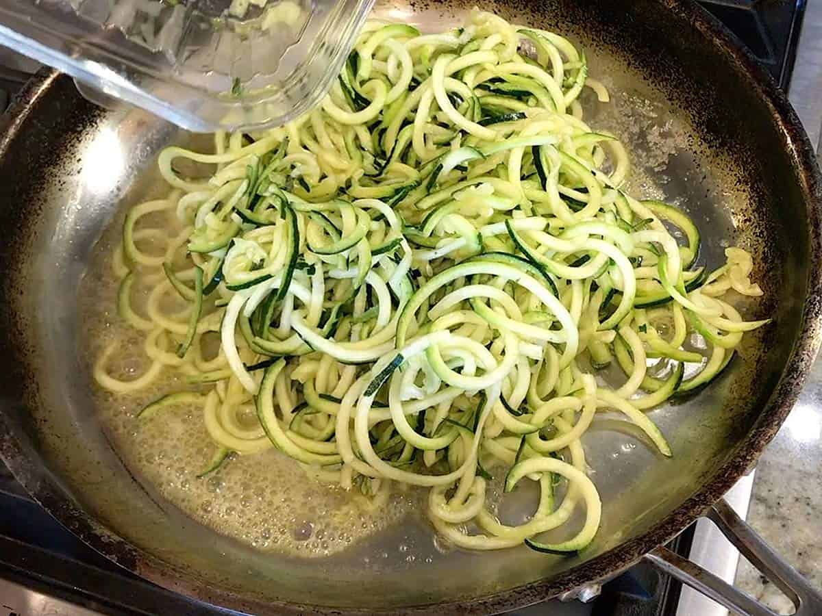 Adding zoodles to melted butter in skillet. 