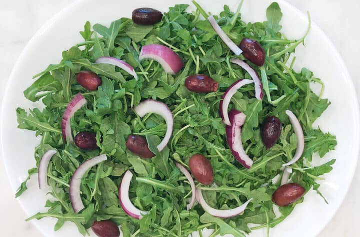 Arugula, red onions, and olives arranged on a plate.
