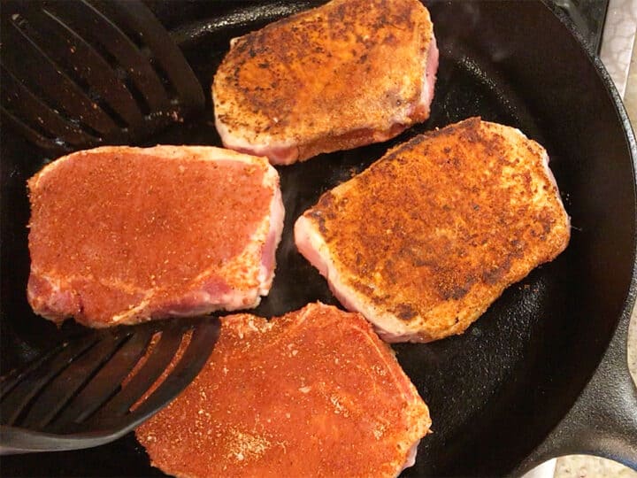 Searing pork chops in a cast-iron skillet.