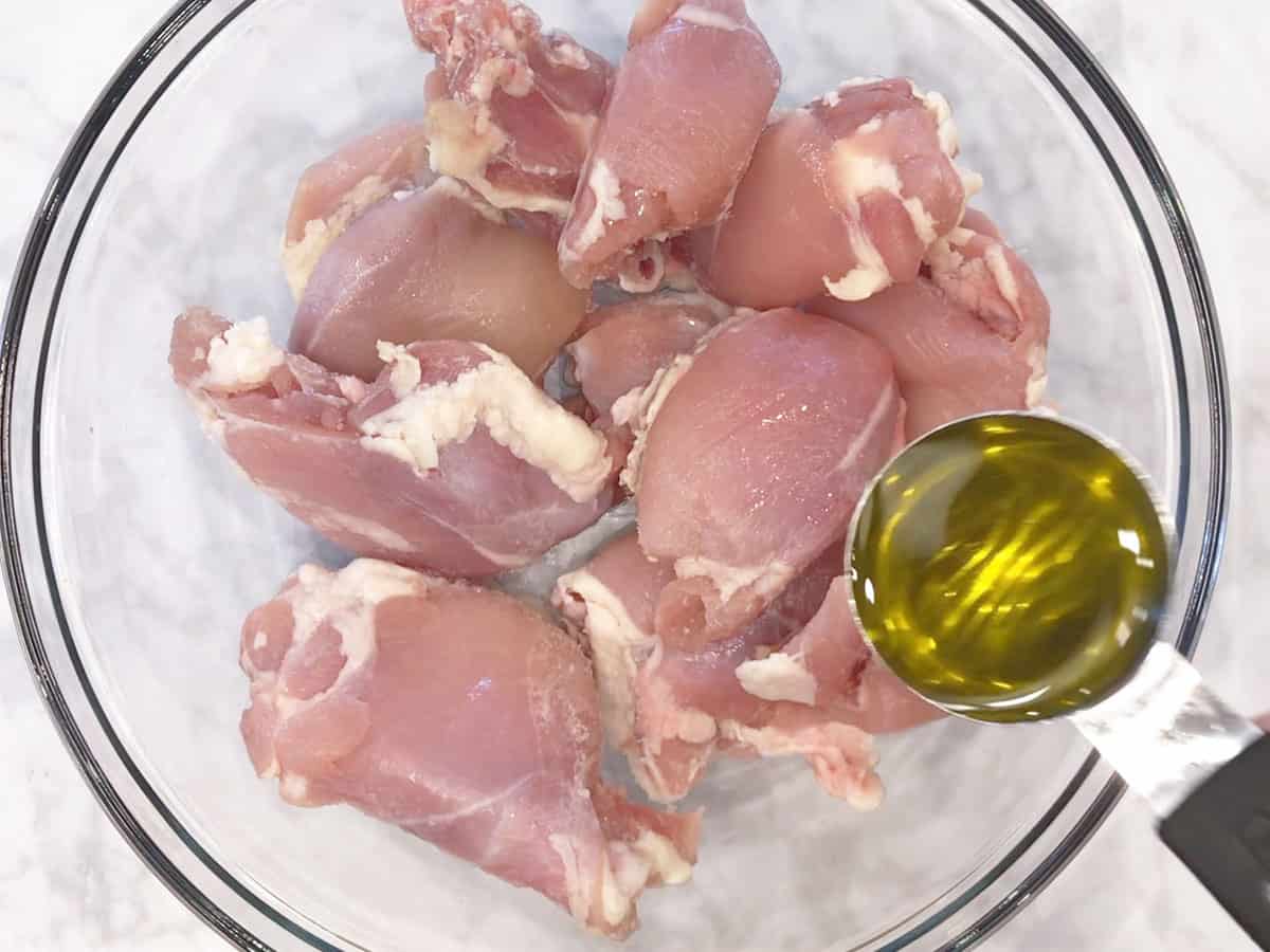 Adding oil to boneless chicken thighs in a bowl.