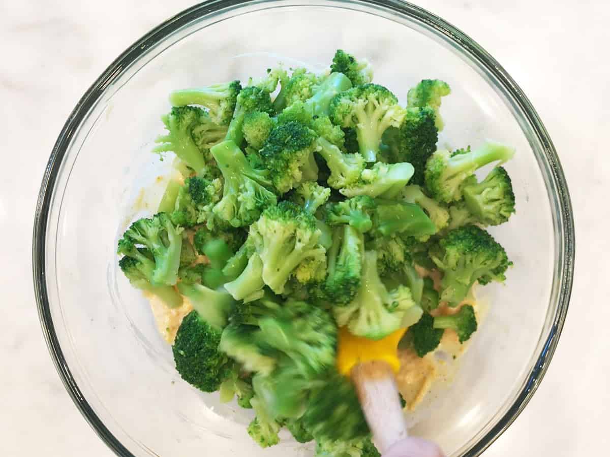 Adding broccoli to cheese sauce in a bowl. 