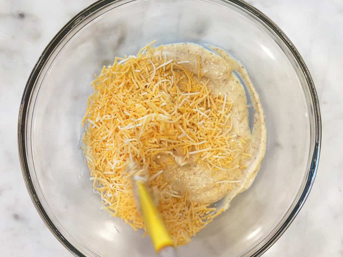 Adding shredded cheese to the sauce. 