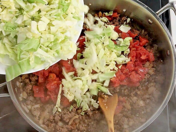 Adding tomatoes and cabbage to the skillet.