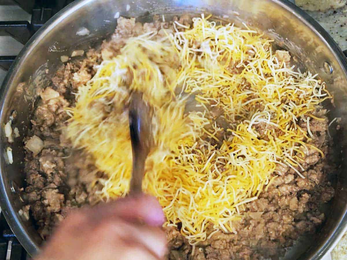 Adding shredded cheese to the beef mixture in the skillet. 
