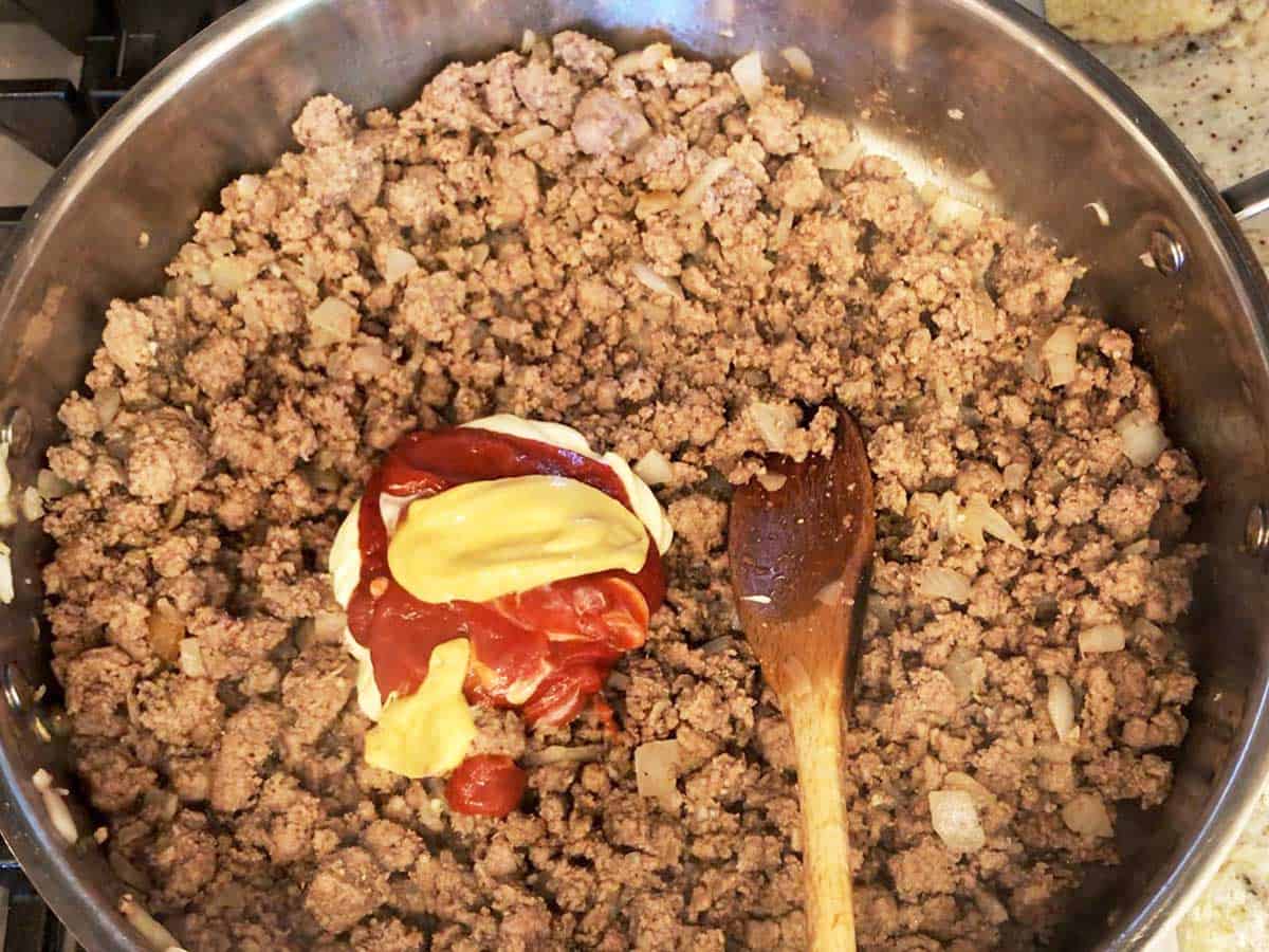Adding condiments to the beef mixture in the skillet. 