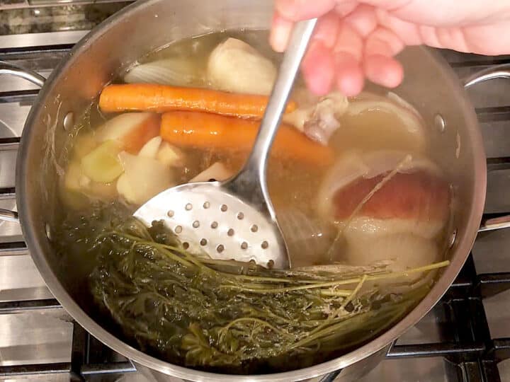 Removing the solids from the broth.
