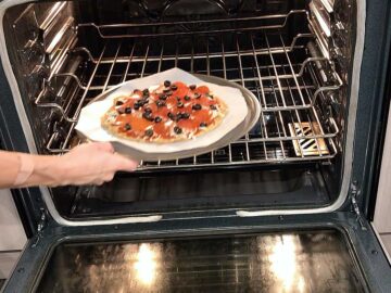 Returning the pizza to the oven to melt the cheese.