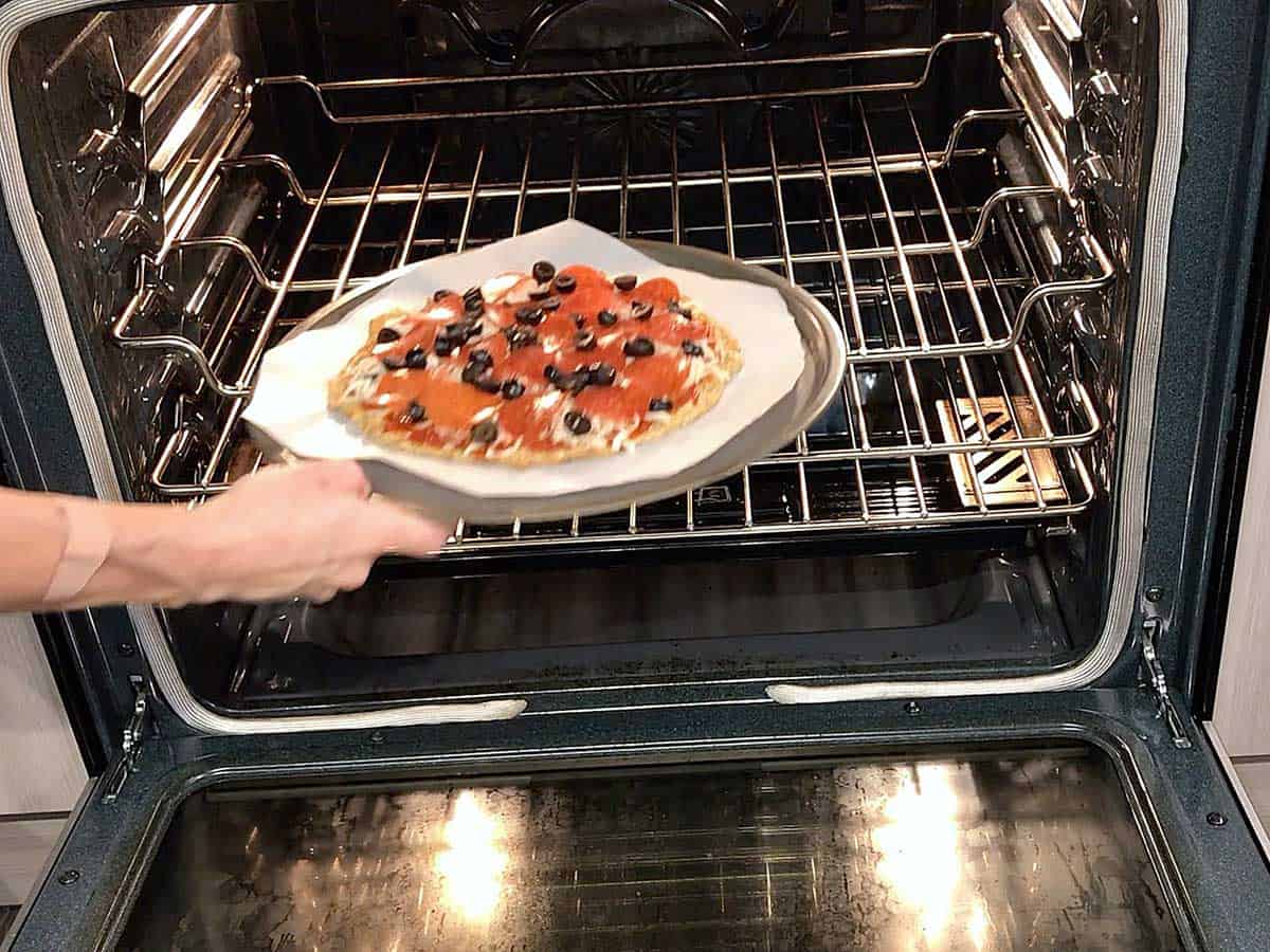 Placing the pizza back in the oven to melt the cheese. 