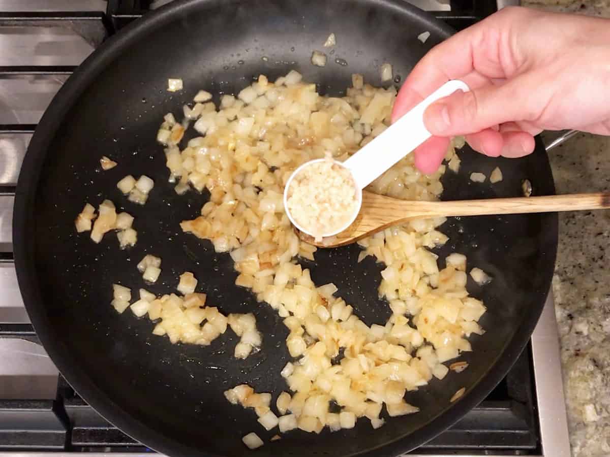 Adding garlic to sauteed onions in pan.