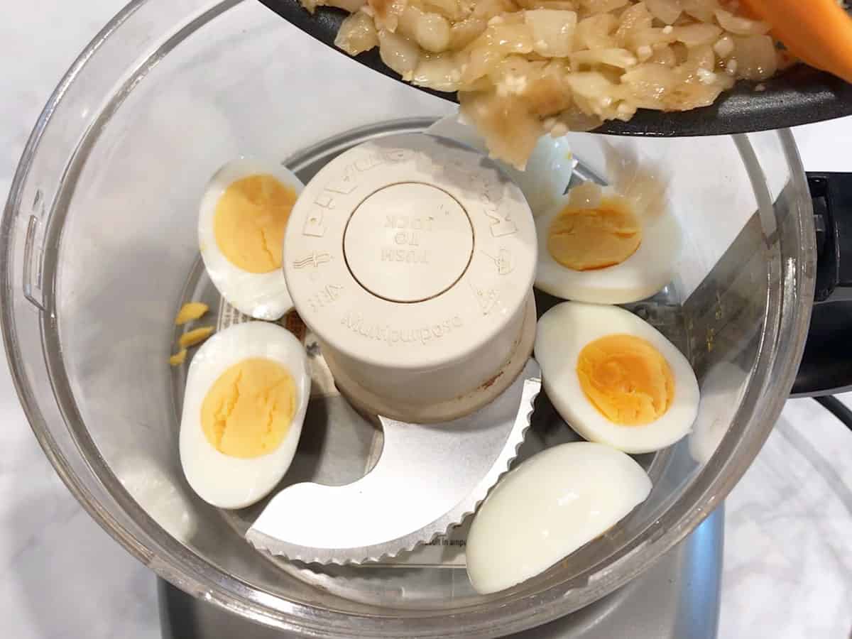 Adding sauteed onions to food processor. There are hard-boiled eggs in the food processor.