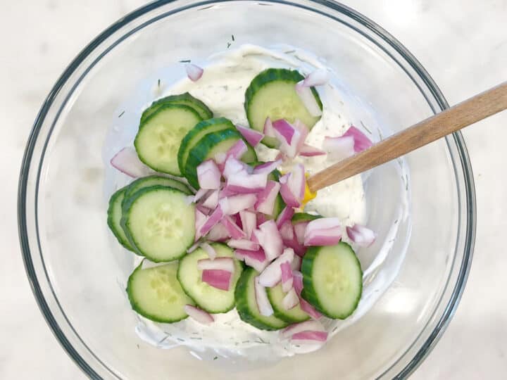Adding cucumber slices and chopped red onion to the dressing.