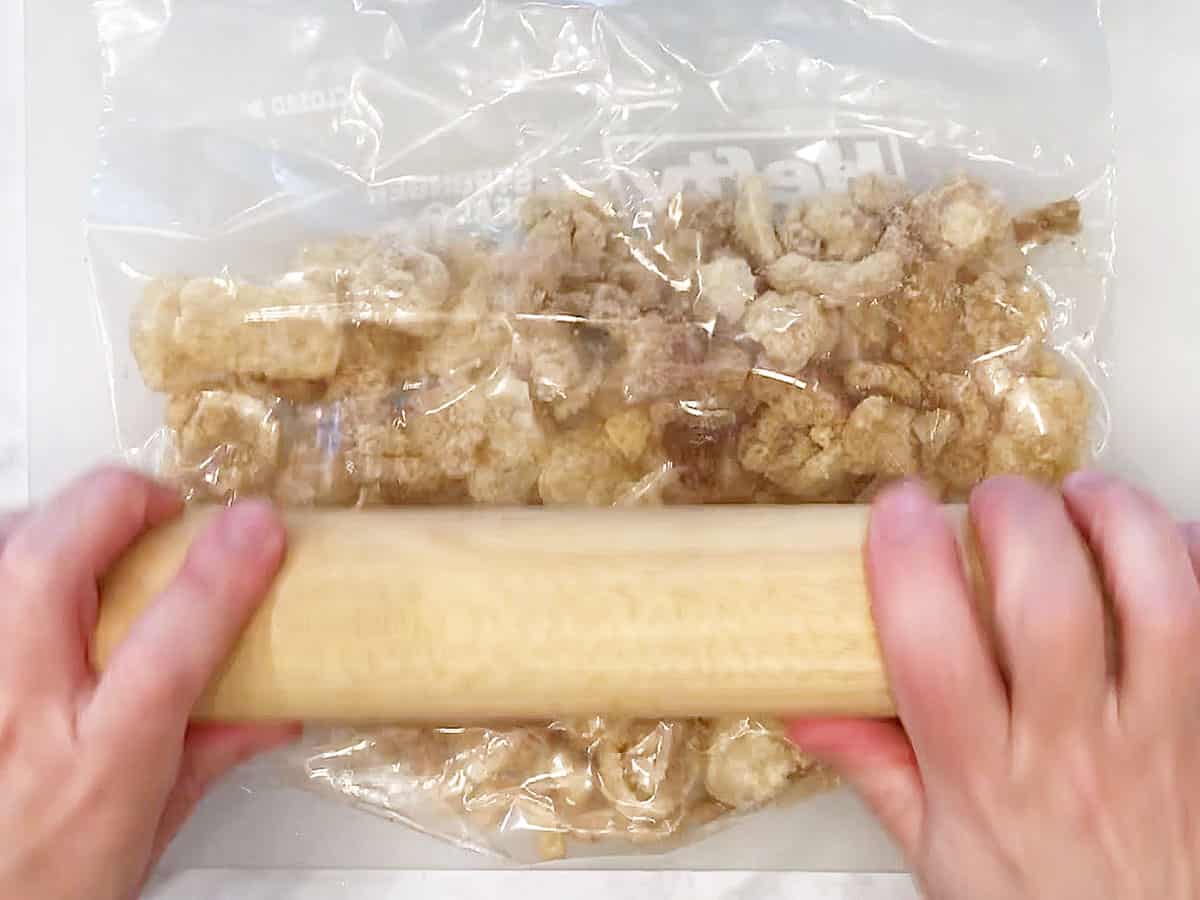 Crushing pork rinds with a rolling pin.