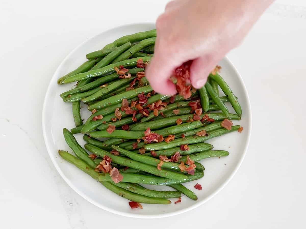 Topping the green beans with cooked chopped bacon.