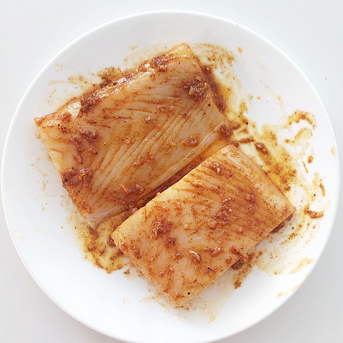 Two raw halibut fillets are coated with an olive oil sauce. 