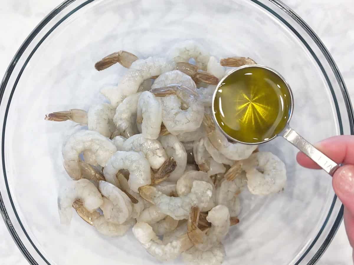 Adding olive oil to shrimp. 