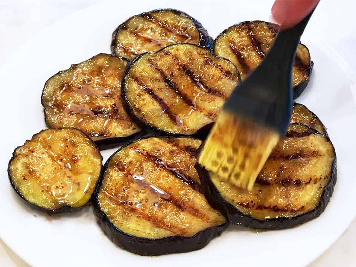 Brushing the grilled eggplant slices with the remaining marinade.