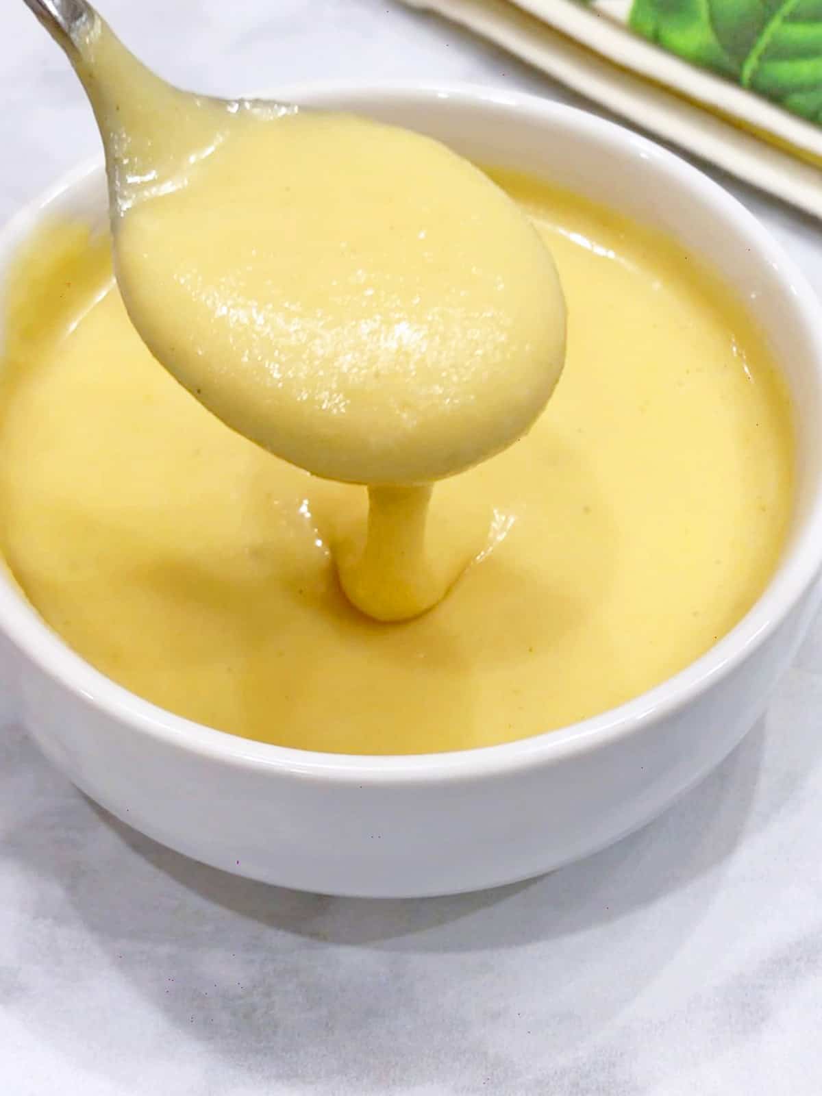 A spoon dipped into hollandaise sauce. 