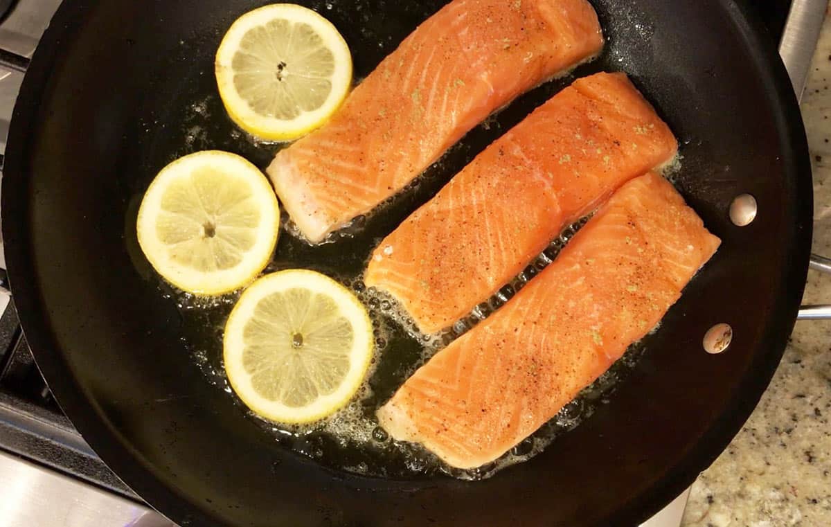Salmon fillets and lemon slices cooking in a skillet. 