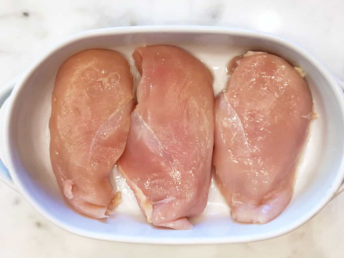 Three raw chicken breasts in a pan.