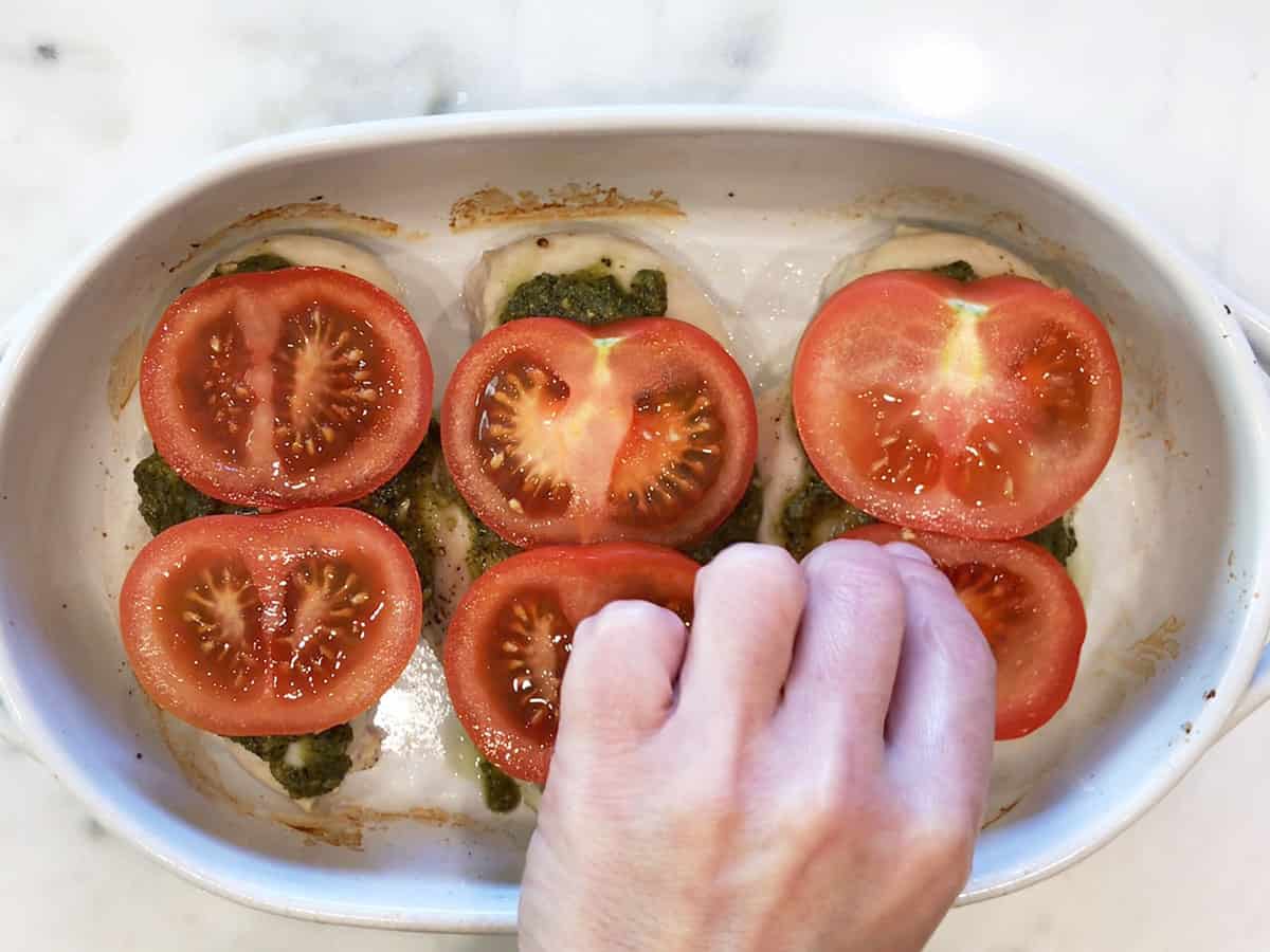 Topping pesto chicken with sliced tomatoes.