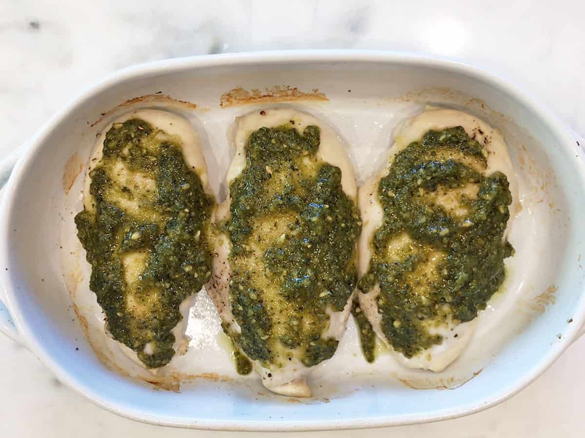 Chicken breasts in a pan, topped with pesto.