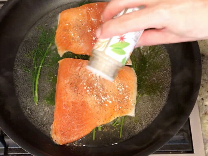 Seasoning the salmon in the skillet.