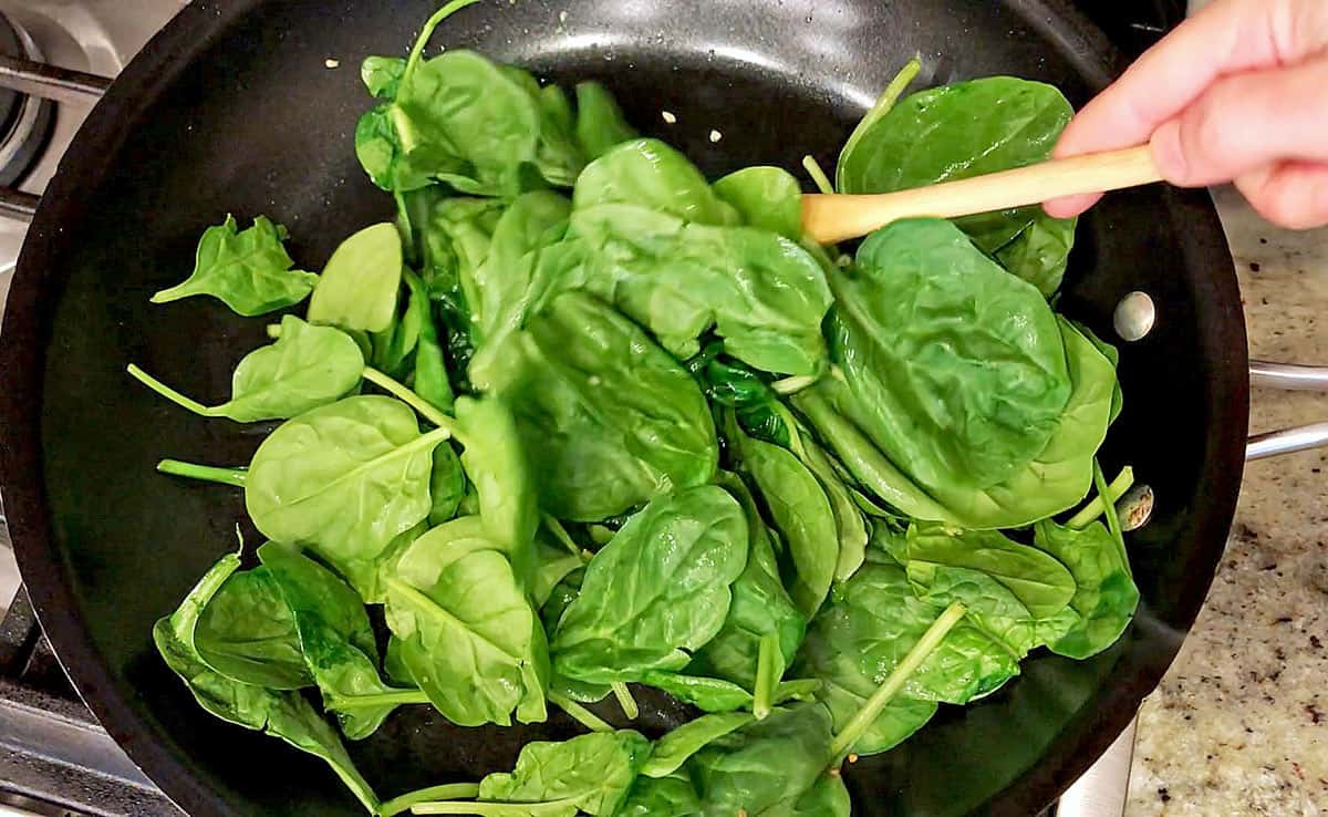 Adding raw spinach leaves to the skillet.