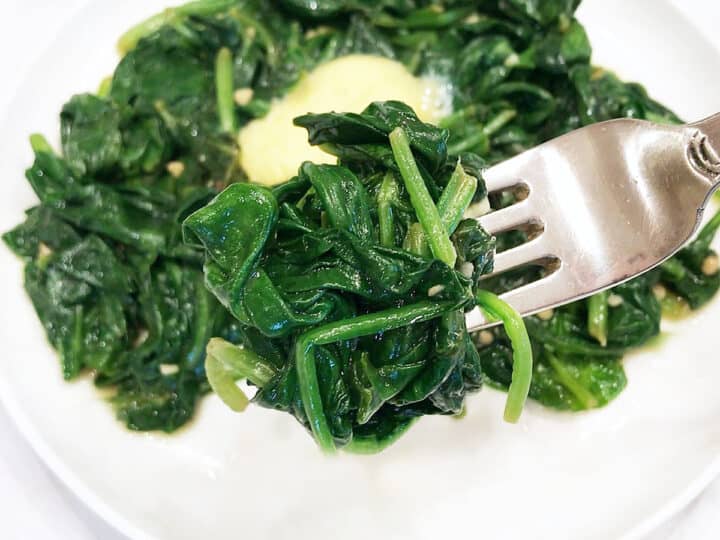 Sauteed spinach lifted from the plate with a fork.