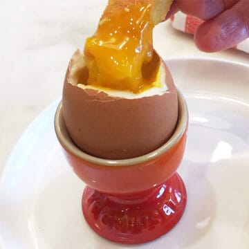 A piece of bread is dipped into the runny yolk of a soft-boiled egg.