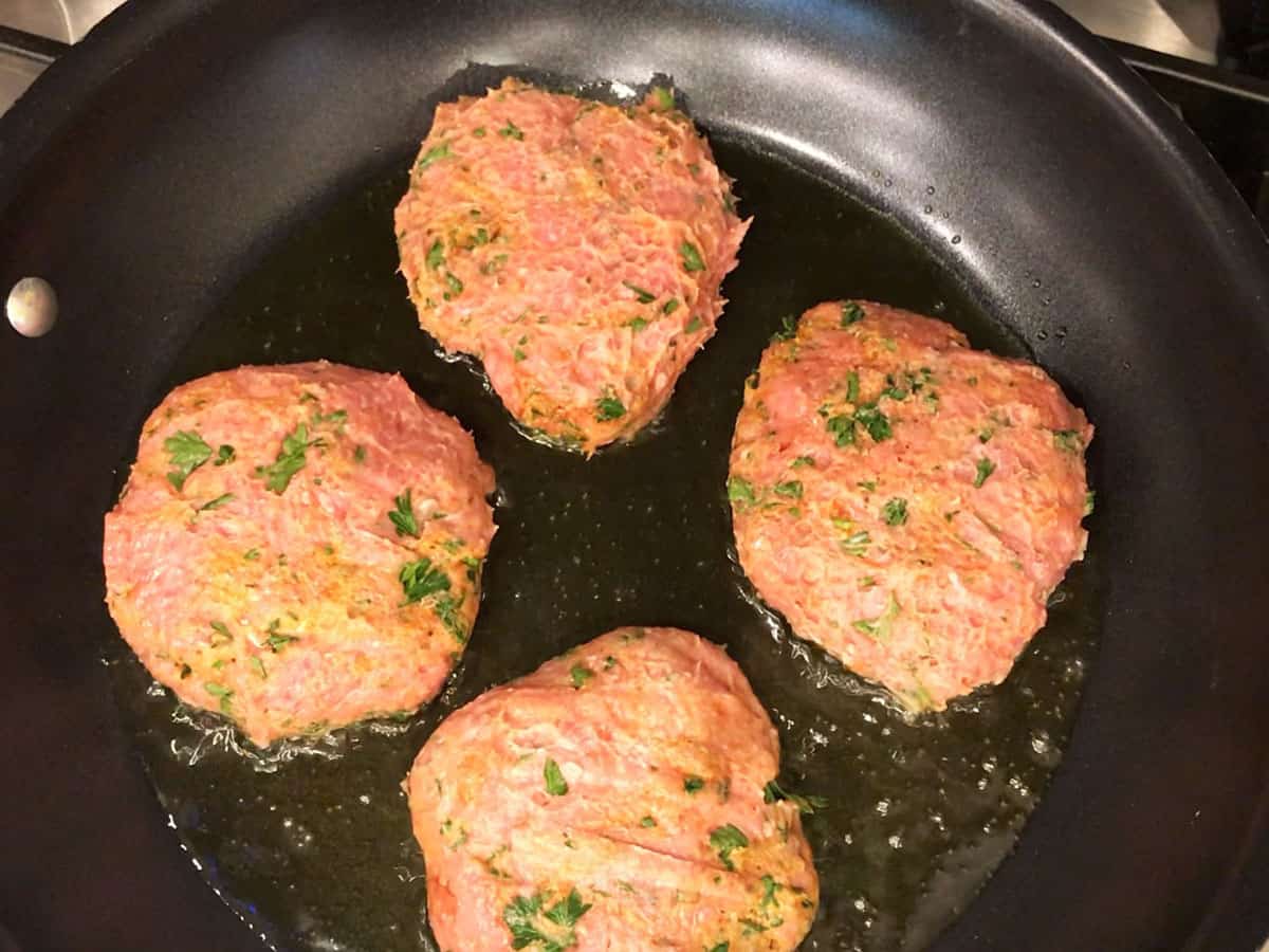 Turkey burgers cooking in a skillet. 